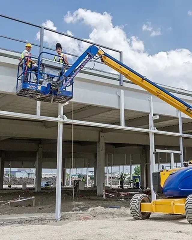 Dos operarios en un brazo articulado trabajando en la estructura de una cubierta