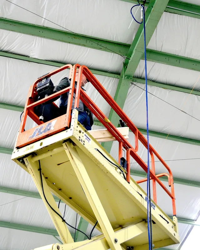 Operario trabajando en el techo de una nave desde una plataforma de tijera